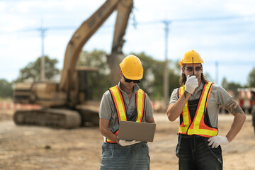 Two construction workers in hard hats and reflective vests discussing blueprints at an industrial site, emphasizing collaboration, planning, and safety in civil engineering projects.