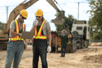 Two construction workers in hard hats and reflective vests discussing blueprints at an industrial site, emphasizing collaboration, planning, and safety in civil engineering projects.