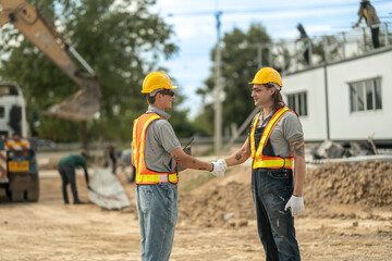 Two construction workers in hard hats and reflective vests discussing blueprints at an industrial...