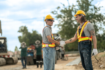 Two construction workers in hard hats and reflective vests discussing blueprints at an industrial...