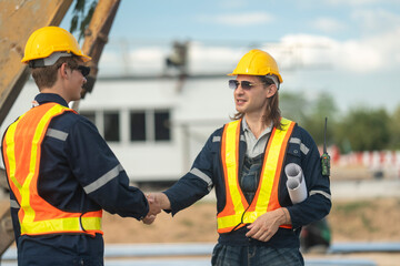 Two construction workers in hard hats and reflective vests discussing blueprints at an industrial...