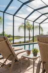 Lounge chair beside blue swimming pool in suburban Florida home with screened enclosure and palm...