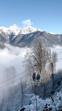Cable cars glide above a frosty forest with snow-covered mountains and clouds. Gabala, Azerbaijan