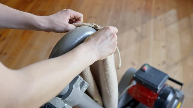 Person&rsquo;s hands replace the sanding waste bag on a floor sanding machine in a room with pine wooden floor, showing the maintenance process and details of the tool, clear light, static camera, close up