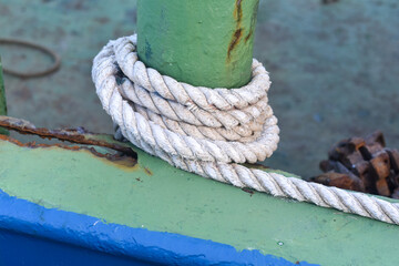 white rope on an iron pole. A thick white rope is wrapped around a green metal bollard, securing a...