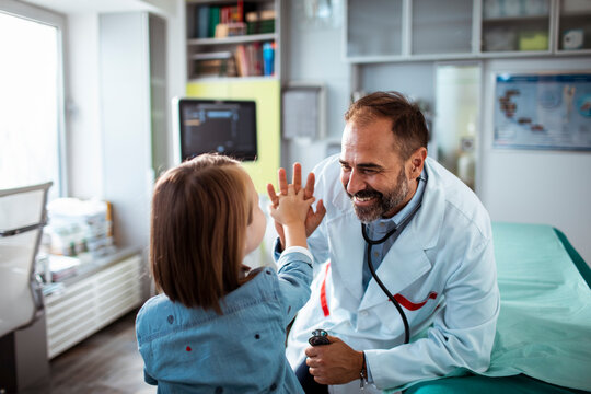 Happy pediatrician giving high five to child patient during doctor visit in medical clinic