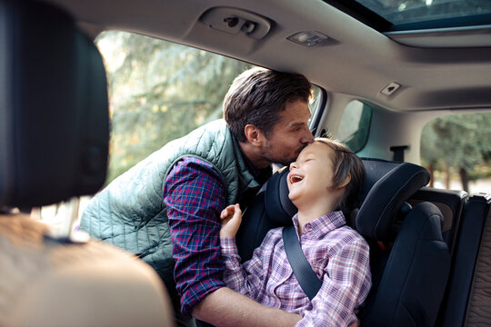 Father kissing little daughter on forehead while adjusting her seatbelt in car
