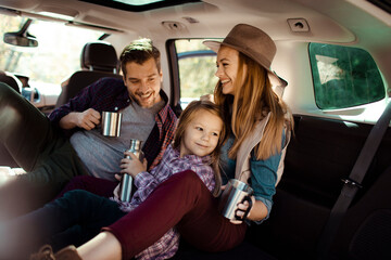 Happy family road trip relaxing in the back of a car with drinks