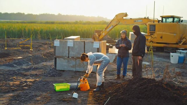 Researchers conducting a soil analysis at a construction site during sunrise, with machinery in the background