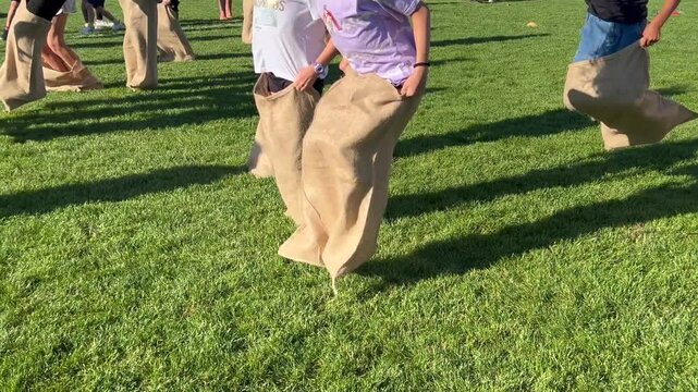 Unrecognizable children traditional potato sack race a competitive game in which participants place both of their legs inside a potato sack hop forward from a starting point toward a finish line.