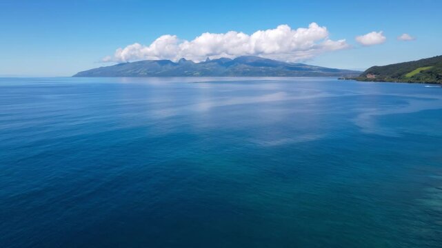 High drone shot tiying over shoreline toward the open ocean in Tahiti, with distant mountains visible across the horizon.