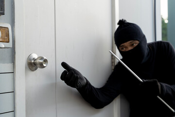Burglar in black clothes attempting to break into a house with a crowbar during a theft or home invasion crime