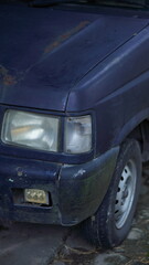 Close-up of a weathered dark-colored minivan's front end, showing signs of age and wear.