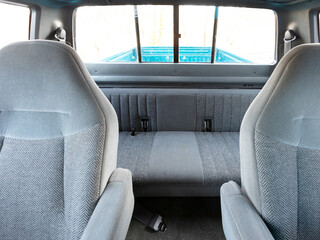 Rear seat interior of an older American pickup truck with extended cab design. Gray cloth bench seats and backrest shown in natural daylight, highlighting clean and well-preserved cabin details