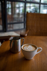 A cup of hot latte with froth art and a jar on wood table	