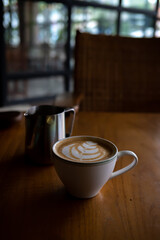 A cup of hot latte with froth art and a jar on wood table	