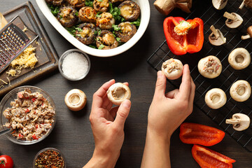 Stuffed mushrooms, kitchen board, ingredients and hands on wooden background, top view