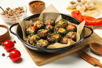 Stuffed mushrooms in frying pan, kitchen board and ingredients on white background, close up