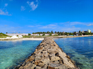 Breakwater extending into clear, turquoise ocean water, with the seabed visible beneath. White...