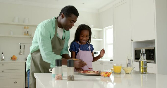 African American, Father and daughter making pizza together in kitchen, enjoying family time