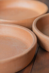 Georgian ketsi on a wooden table. Ketsi, traditional handmade unglazed ceramic cookware, clay round frying pan, dish, plate, pot, all in one, close-up, high resolution.