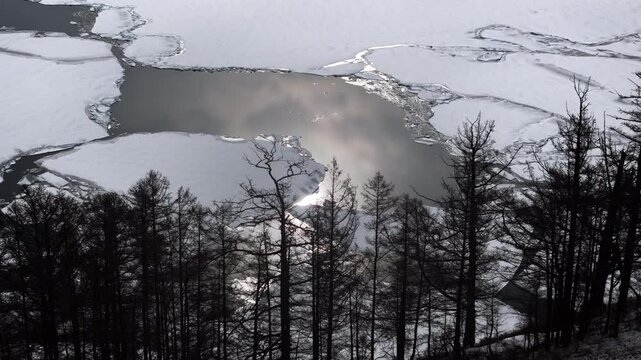 Aerial drone view of a lake with floating ice floes and forest on the shore