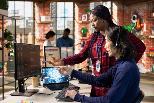 Call center supervisor guiding intern on how to use AI chatbot app on computer. African american customer support workplace onboarding specialist teaching man to use artificial intelligence software - Powered by Adobe