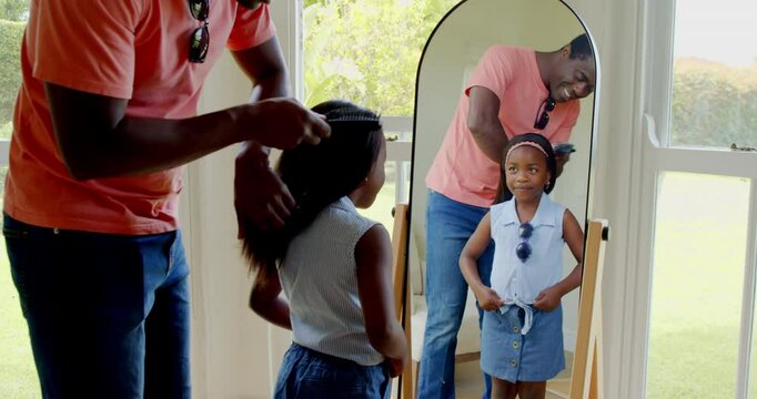 African American, Father brushing daughter's hair at home, both smiling in front of mirror