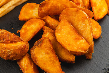 Crispy potato wedges served on a black plate