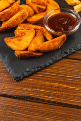 Crispy potato wedges served with dipping sauce on wooden table