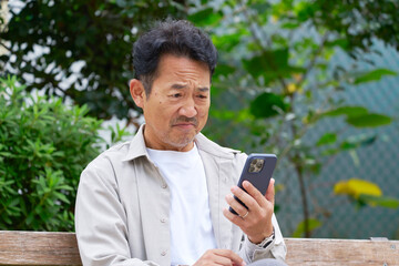 Fototapeta premium 悩まみながら屋外でスマートフォンを見る中年の男性 屋外