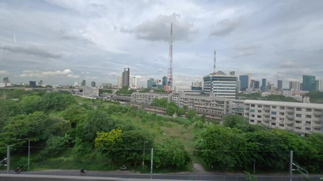view from the window of an SRT Red Line train in Bangkok, Thailand. The passing scenery includes various urban elements such as residential buildings, commercial structures, other railway tracks