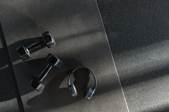 Black dumbbells for sports and acoustic headphones lie on the floor in the gym on a stylish yoga mat