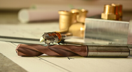 Metal drill bits, milling cutters and a caliper are laying on a technical drawing