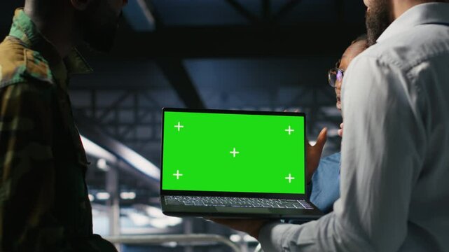 Military command center engineering team using chroma key notebook. Army IT expert and coworkers in data center using green screen laptop to defend networks against threats, camera B