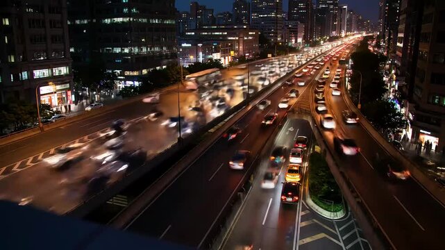 Aerial or high-angle view of heavy traffic on a multi-lane city highway during nighttime. Blurred car lights and fast-moving vehicles create a dynamic motion effect, showcasing the nonstop activity 