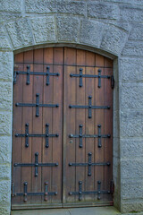 A weathered wooden door with robust iron hardware stands within a sturdy stone archway. Iron hinges form bold cross shapes across the panels. Time and weather leave marks that add to its strength.