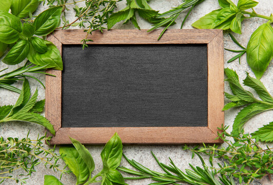 Fresh herbs framing empty chalkboard on gray stone background