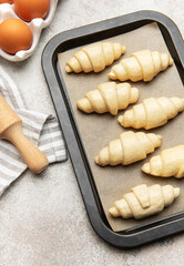 Freshly made croissants resting on baking sheet await oven's warm embrace