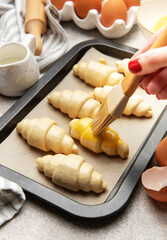 Baker brushing egg yolk on raw croissants on baking sheet