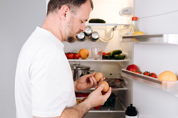 Man inspecting fresh eggs in refrigerator while preparing for a nutritious breakfast, surrounded by...