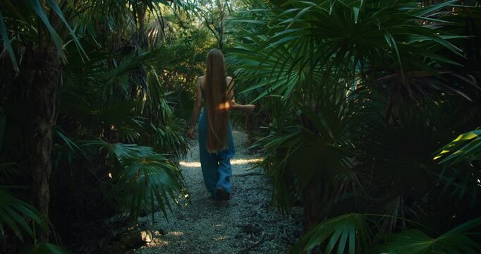 Woman walking barefoot along tropical forest path with long hair trailing behind