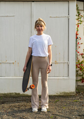 Modern young woman with skateboard standing against wooden background. Dressed in light casual...