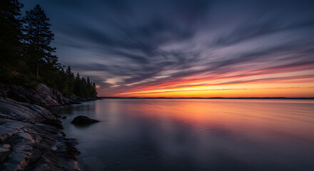 Stunning Vibrant Sunset over Calm Water with Silhouetted Trees and Rocky Shore