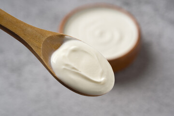 Top view of yogurt on wooden spoon with yogurt in bowl in background