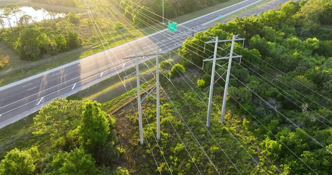 Power lines on tall steel pylons extend over highway with fast driving cars. Electricity transmission infrastructure in busy area.