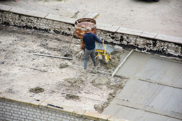 A builder on the roof makes repairs with a concrete screed, transports mortar with a wheelbarrow, roof insulation. High quality photo