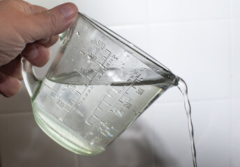 Measuring cup pouring water with precision, captured mid-action to highlight kitchen tools, liquid measurement, hydration, and culinary preparation.