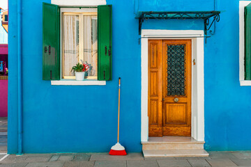 A blue house with green shutters and orange wooden door in Burano, Italy.