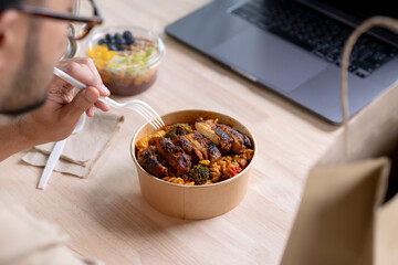 Young Asian man eating healthy meal while working, Businessman having a lunch break at the office, focus on food